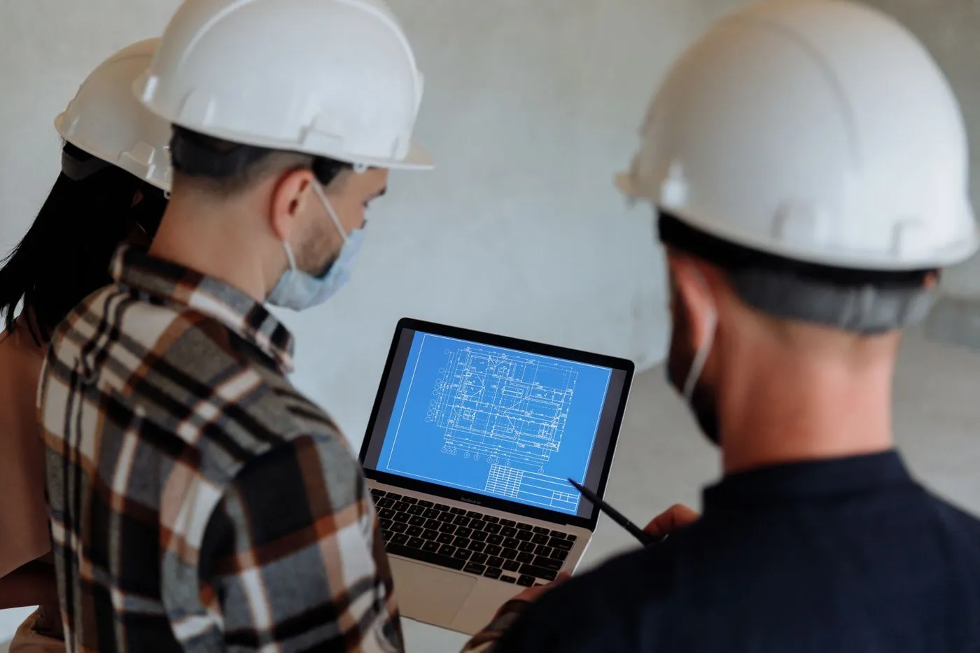 Engineers in hard hats reviewing a project plan on a laptop