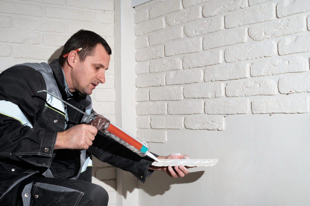 Thermal & Moisture Protection Estimating Services 2 Master applies glue tiles for facing the house. The master builder decorates the walls of the apartment. Finishing the building with modern materials.